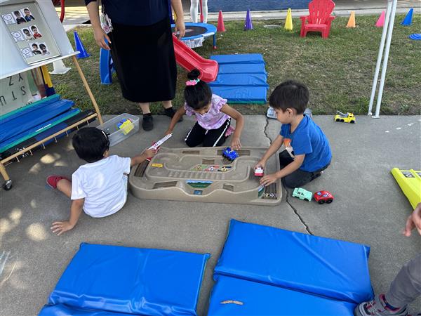 three students playing with fire trucks during their outdoor time.